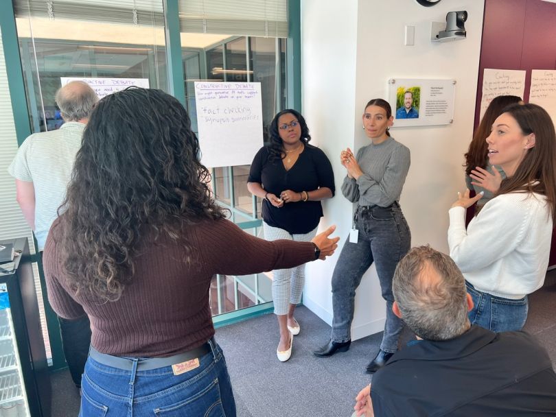 Udemy employees stand discussing ideas near a wall with their meeting notes. 